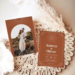 Peut inclure: Deux faire-part de mariage couleur terre cuite avec un motif de soleil. L'un pr&eacute;sente une photo d'un couple, l'autre porte les noms "Aubrey & Oliver" et les d&eacute;tails du mariage. Les invitations sont sur un dessous de plat tiss&eacute;.
