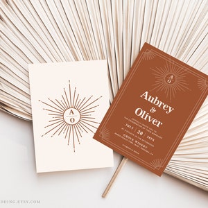 Peut inclure: Deux cartons d'invitation de mariage avec un motif de soleil. L'un est blanc cass&eacute; avec un soleil et les initiales "AO". L'autre est de couleur rouille avec les noms "Aubrey & Oliver" et les d&eacute;tails du mariage. Les cartes sont sur un fond neutre.
