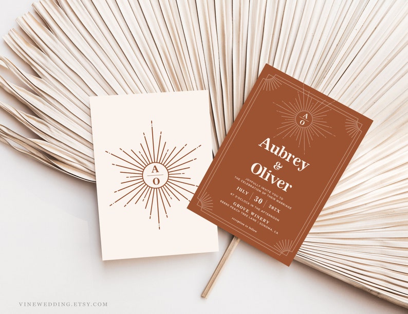 Peut inclure: Deux cartons d'invitation de mariage avec un motif de soleil. L'un est blanc cass&eacute; avec un soleil et les initiales "AO". L'autre est de couleur rouille avec les noms "Aubrey & Oliver" et les d&eacute;tails du mariage. Les cartes sont sur un fond neutre.