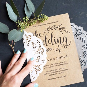 K&ouml;nnte beinhalten: Eine braune Papier-Hochzeitseinladung mit wei&szlig;er Spitzen&uuml;berlagerung. Die Einladung lautet "Sie sind eingeladen, die Hochzeit von Lynn & Joshua zu feiern" und enth&auml;lt Datum, Uhrzeit und Ort der Hochzeit.