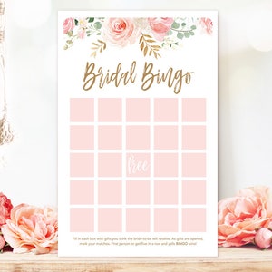 May include: A Bridal Bingo game card with a floral design. The top of the card features pink and gold flowers. The words "Bridal Bingo" are in gold script. The card has pink squares for game play and the word "free".