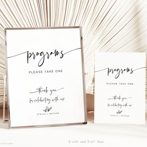 May include: Two white signs with black text that say "programs please take one" and "thank you for celebrating with us! Stella + Nathan". The signs are in a silver frame and on a white surface.
