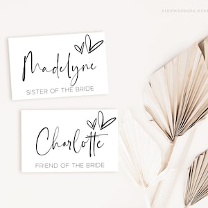 May include: Two white cards with black text and hearts. The top card says "Madelyne Sister of the Bride". The bottom card says "Charlotte Friend of the Bride".