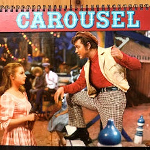 Puede incluir: Un cartel de película vintage para el musical "Carousel" con un hombre y una mujer con ropa de época de pie frente a un carrusel. El hombre lleva una camisa roja, una chaqueta blanca y un sombrero. La mujer lleva un vestido rosa. El cartel tiene un fondo rojo con la palabra "Carousel" en letras blancas.