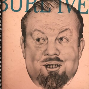 Puede incluir: Una portada de álbum de vinilo vintage con una ilustración en blanco y negro de la cara de un hombre con barba de chivo. El título del álbum es "The Wayfaring Stranger" y el artista es "Burl Ives". La portada del álbum enumera varias canciones, entre ellas "Ther-Winged Bat", "Sweet Betsy From Pike", "On Top Of Old Smoky", "Cowboy's Lament", "Riddle Song", "How Where I'm Going", "I Know My Love", "Wee Cooper O'Fife", "Colorado Trail", "Roving Gambler", "Bonnie Wee Lassie", "The Div", "On Springfield Mountain", "Little Mohee", "Peter Gray", "Robin, He Married".