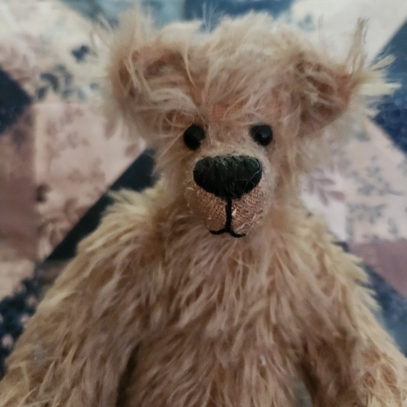 May include: A close-up of a light brown teddy bear with a black nose and button eyes. The bear has a shaggy, fluffy coat.