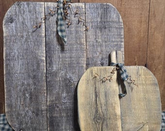 May include: Two pumpkin-shaped wooden plaques made from weathered gray and tan reclaimed wood planks. Each plaque features a small wooden stem at the top, tied with a dark green and navy plaid fabric ribbon and decorative brown wire tendrils.