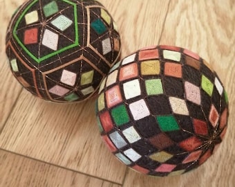 May include: Two colourful, geometrically patterned Japanese hand-sewn balls called "Temari" with intricate embroidery. The balls are made of fabric and thread and feature a variety of colours, including red, green, brown, and pink.