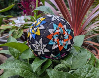May include: A colourful, hand-stitched Japanese sphere called a "Temari" with a black background and intricate star patterns in shades of blue, yellow, red, and white.