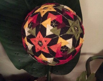 May include: A colourful, geometric patterned ball with red, orange, yellow, green, and white accents. The ball is made of fabric and is a traditional Japanese craft.
