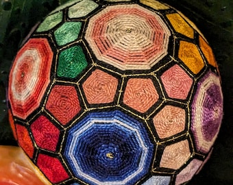 May include: A colourful, geometrically patterned ball with a black background and gold accents. The ball is made of fabric and is stitched together in a complex pattern.