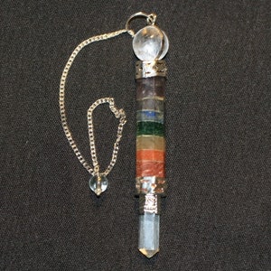 Peut inclure: Une chaîne en argent pend d'une boule de cristal transparente, attachée à un pendule en cristal argenté et multicolore. Le pendule est composé de sept pierres de couleurs différentes, dont le rouge, l'orange, le jaune, le vert, le bleu, l'indigo et le violet.