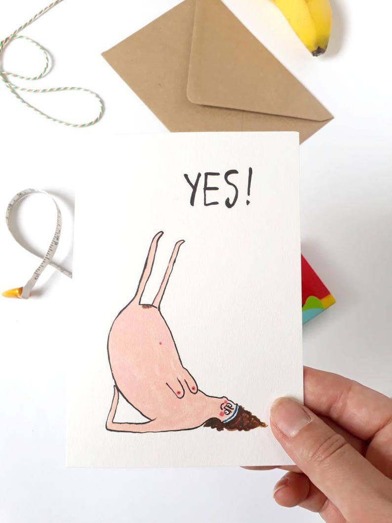 May include: A white card with a hand-drawn illustration of a person doing a yoga pose. The person is pink with brown hair and is wearing a blue headband. The text "YES!" is written in black at the top of the card.