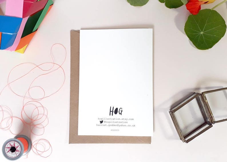 May include: A white card with brown paper backing. The card has black text that reads "HOG" and includes contact information for the artist. The text reads "hogillustration.etsy.com", "@hogillustration", and "harriet_godden@yahoo.co.uk".