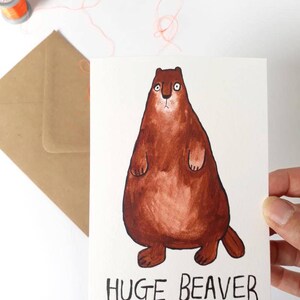 May include: A greeting card with a cartoon illustration of a brown beaver. The beaver is standing on its hind legs with its paws in the air. The text "HUGE BEAVER" is written below the beaver.