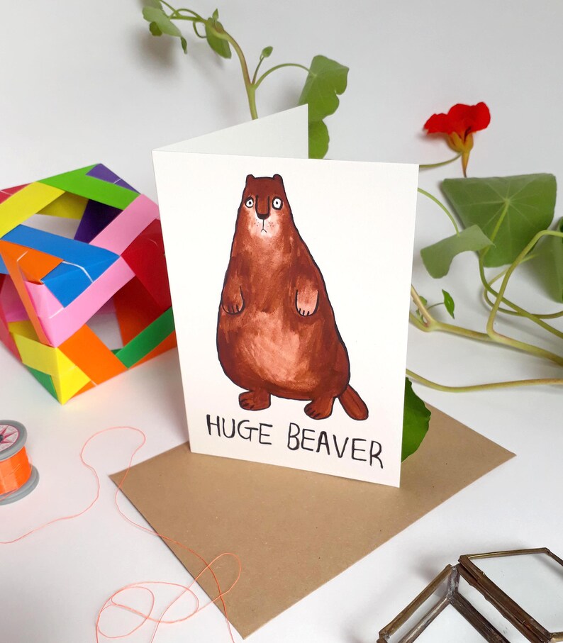 May include: A white card with a brown cartoon beaver on it. The beaver is standing on its hind legs with its paws crossed. The text "HUGE BEAVER" is printed below the beaver.