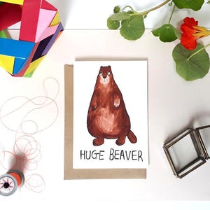 May include: A greeting card with a cartoon illustration of a brown beaver with a white belly and the text "HUGE BEAVER" in black.