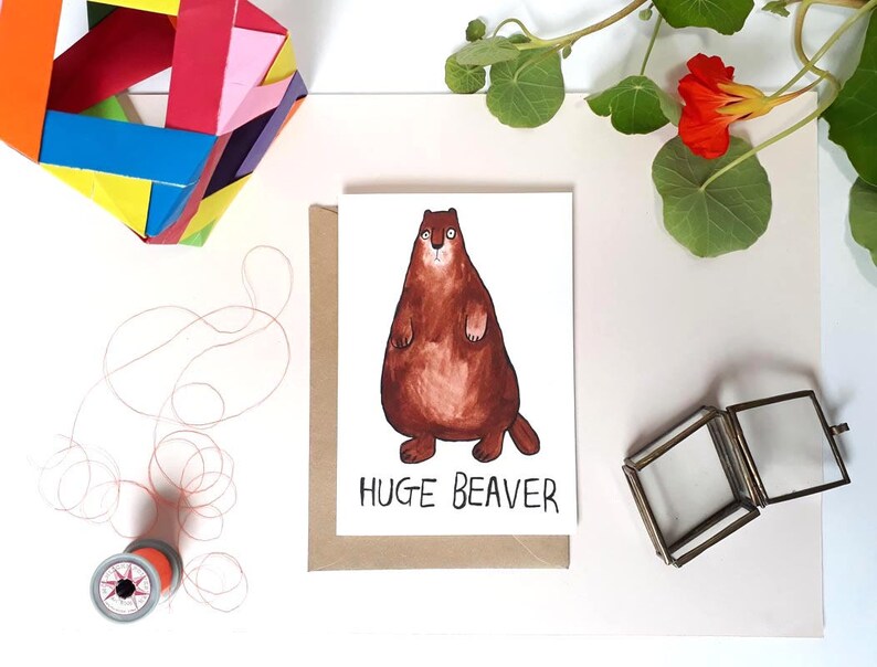 May include: A greeting card with a cartoon illustration of a brown beaver with a white belly and the text "HUGE BEAVER" in black.