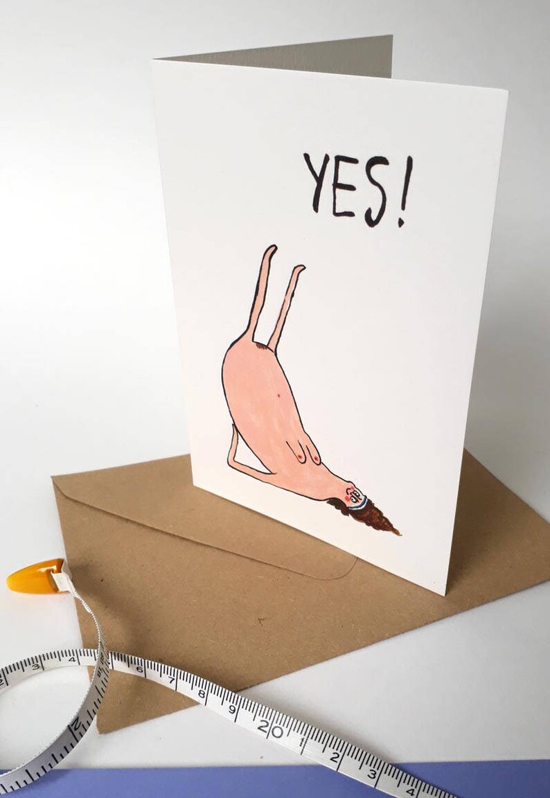 May include: A white card with a pink cartoon figure doing a yoga pose with the word "YES!" written in black above it.