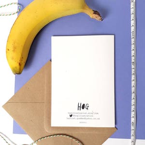 May include: A white card with black text that reads "HOG" and includes contact information for the artist. The card is on a brown envelope with a blue background. A yellow banana is in the upper left corner of the image.