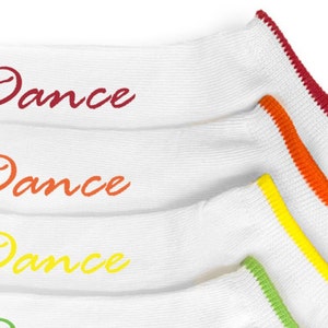 May include: Four pairs of white socks with colorful trim. Each sock has the word "Dance" written on it in a different color: red, orange, yellow, and green.