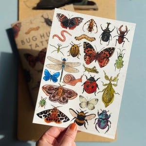 Peut inclure: Une feuille de tatouages temporaires d'insectes et de papillons colorés. La feuille présente une variété d'insectes, notamment des papillons, des mites, des scarabées, des libellules et un escargot. Les tatouages sont parfaits pour ajouter une touche de fantaisie à votre look.