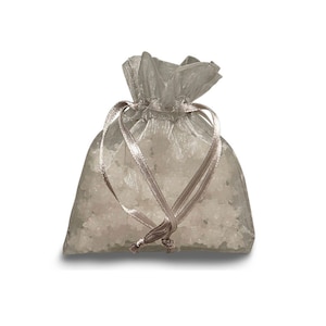 Puede incluir: Una bolsa de organza plateada con cierre de cordón blanco. La bolsa está llena de cristales blancos.