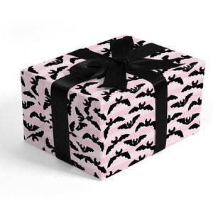 May include: A pink and black gift box with a black ribbon. The box is wrapped in wrapping paper with a pattern of black bats on a pink and white striped background.