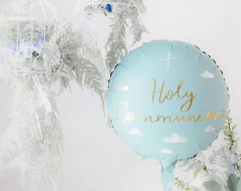 以下が含まれることがあります： 「Holy Communion」の金色の文字、十字架、雲のイラストが描かれた、水色の丸い風船。白いフラワーアレンジメントと装飾的な鳥かごに囲まれています。