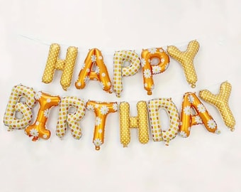May include: Gold foil balloons spelling out "Happy Birthday" with a white daisy pattern.