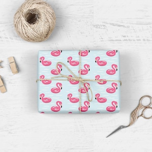 May include: Light blue gift wrap with a repeating pattern of pink flamingo pool floats. The gift is wrapped with twine and tied with a bow.
