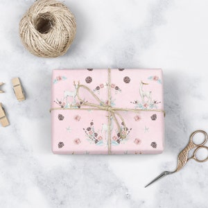 May include: A pink gift box with a white deer and floral pattern wrapped with twine. The box is sitting on a white marble surface.