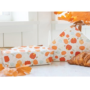 以下が含まれることがあります： カボチャ模様の装飾ボックス2つ。ボックスは白で、オレンジ、赤、水色のカボチャと緑の葉が描かれています。クロワッサンと秋の葉も画像にあります。