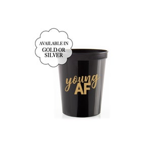 Puede incluir: Vaso de plástico negro con el texto "young AF" en letras doradas. Disponible en oro o plata.