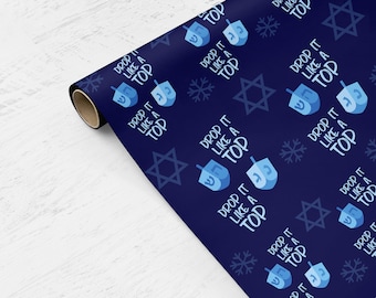 May include: A roll of navy blue wrapping paper with a repeating pattern of blue dreidels, snowflakes, and Star of David symbols. The text "DROP IT LIKE A TOP" is also featured in a repeating pattern.