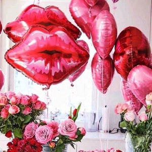 May include: A group of red and pink foil balloons shaped like lips and hearts. The balloons are tied together and floating in the air. There are pink roses in the foreground.