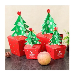 Könnte beinhalten: Rote Geschenkboxen mit weißen Punkten und grünen Weihnachtsbaumaufsätzen. Die Boxen haben eine Rentiergrafik und den Text "MERRY CHRISTMAS HAPPY NEW YEAR". Ein Apfel liegt vor den Boxen.