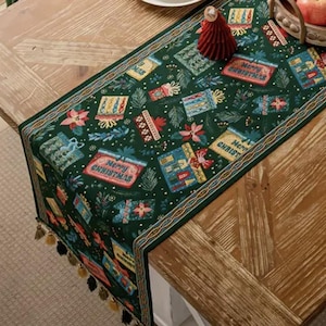 May include: A festive Christmas table runner in dark green with gift box and floral patterns. The runner is adorned with the text "Merry Christmas" and has a fringed edge. A wooden table is set with plates, silverware, and a fruit basket.