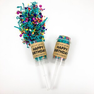 Op de afbeelding: Twee confetti push-pops met bruine labels waarop staat "posh and sparkle HAPPY BIRTHDAY CONFETTI PUSH-POP". De confetti is turquoise, roze, paars en geel.