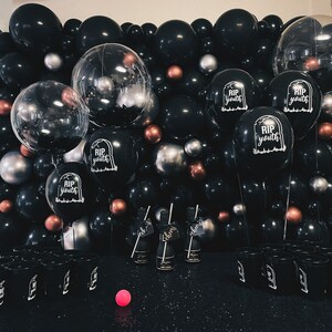 May include: A black and silver balloon arch with the text "RIP youth" on several balloons. There are also black and silver cups in front of the arch.