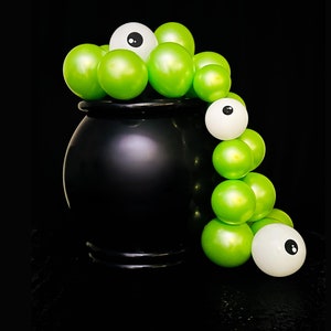 May include: A black cauldron overflowing with green orbs and white eyeballs, creating a spooky Halloween scene. The glossy green spheres and white eyeballs are arranged to appear as if they are spilling out of the cauldron.