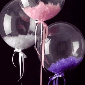 May include: Three clear plastic balloons filled with feathers. The balloons are tied with white, pink, and purple ribbons.