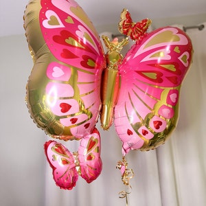 May include: A gold and pink butterfly balloon with red hearts and smaller butterfly balloons attached.