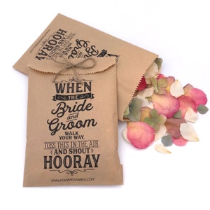 May include: Two brown paper bags with a black and white design that says "When the Bride and Groom walk your way, toss this in the air and shout Hooray!"  The bags are filled with pink, white, and green flower petals.