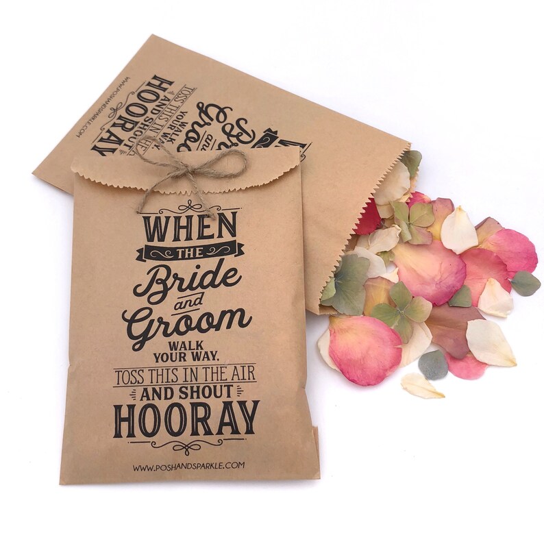 May include: Two brown paper bags with a black and white design that says "When the Bride and Groom walk your way, toss this in the air and shout Hooray!"  The bags are filled with pink, white, and green flower petals.