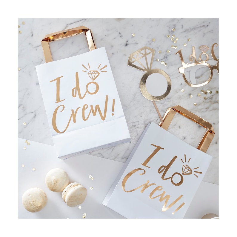 May include: Two white paper gift bags with gold handles and the text "I do Crew!" in gold lettering. Each bag features a gold diamond ring graphic.