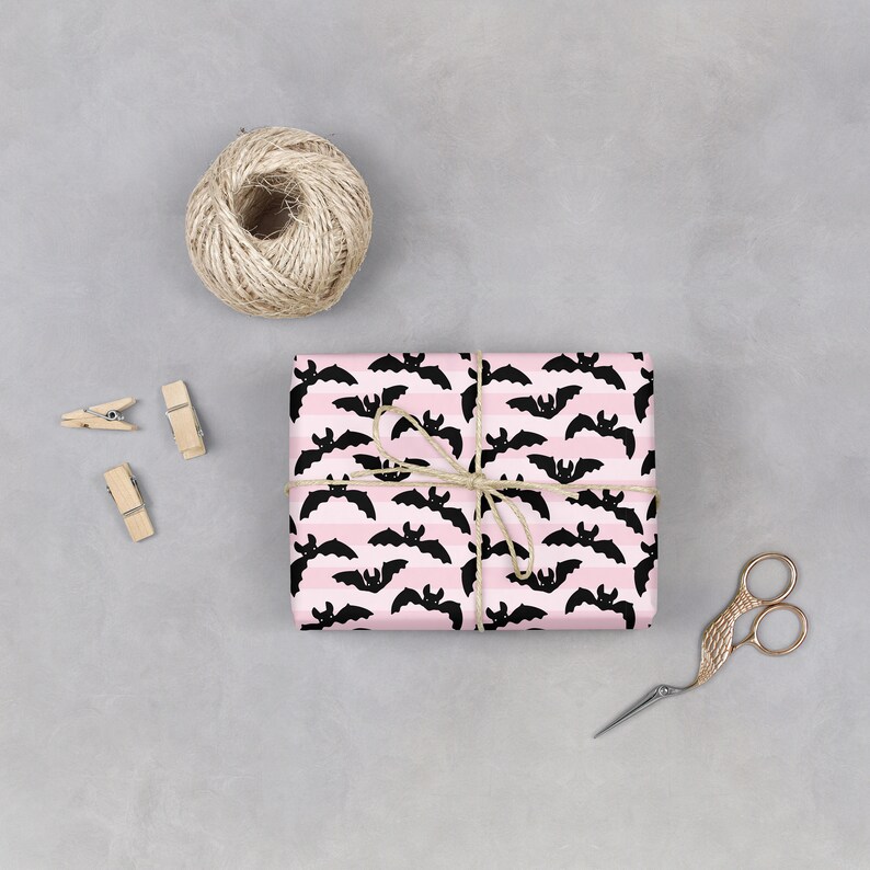 Op de afbeelding: Een roze en zwart cadeaupapier met een patroon van vleermuizen. Het cadeau is ingepakt met touw en vastgebonden met een strik.