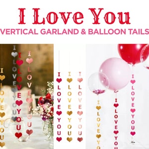 Puede incluir: Un conjunto de guirnaldas de papel rojo, rosa y dorado con las palabras "I Love You" enhebradas en ellas. Las guirnaldas cuelgan de globos, que también están decorados con las palabras "I Love You".