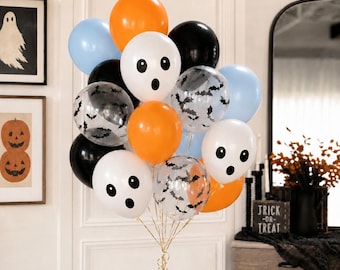 May include: A cluster of Halloween balloons featuring solid orange, black, and light blue colors, alongside white balloons with printed ghost faces and clear balloons decorated with black bat silhouettes, all tied together with gold ribbons.