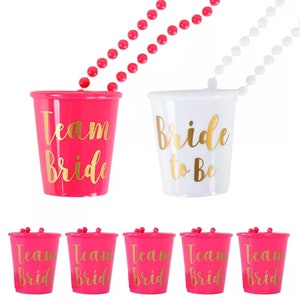 Pu&ograve; includere: Set di sei bicchieri da shot in plastica rosa con scritta dorata "Team Bride". C'&egrave; anche un bicchiere da shot in plastica bianca con scritta dorata "Bride to Be".